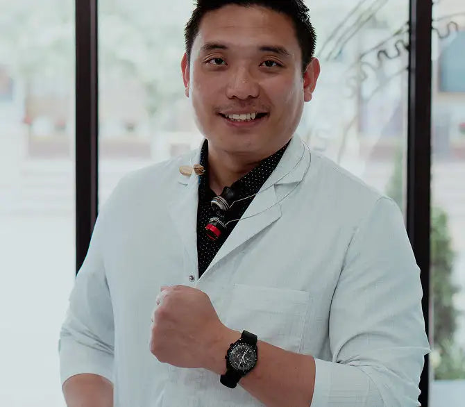 Black watch with a round face and black strap worn on the man’s left wrist.
