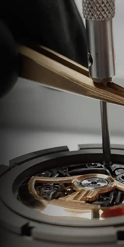 A precision-engineered watch movement with gold-toned gears and a silver dial, being meticulously adjusted by a jeweler’s tool.