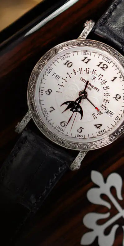 A silver patek philippe watch with a white dial, moon phase display, and black leather strap.